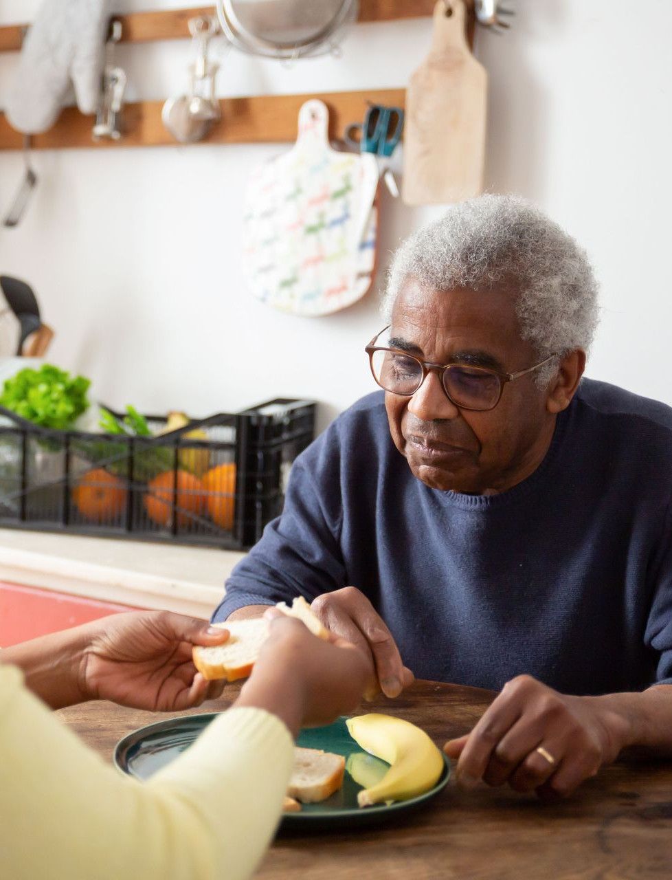 A woman assists an elderly man with meals at home, showcasing care and support.